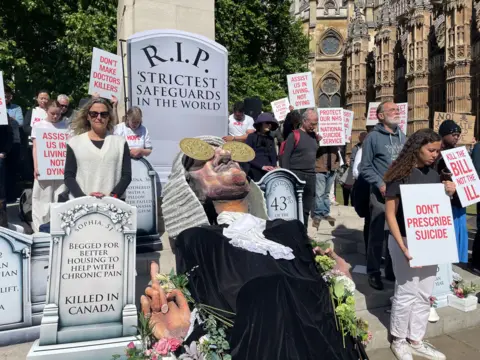 PA Media Protesters opposing the bill gather outside Parliament with placards, a puppet judge and a mock gravestone reading: