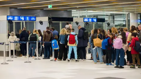 Alamy Travellers with luggage queue at arrivals as officials in booths marked