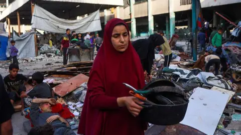 Getty Images A woman salvages useable items from the debris at the Fahmi Al-Jarjawi School in Gaza City on May 26, 2025, following an Israeli strike