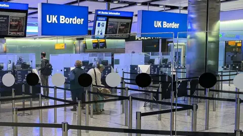 Getty Images People queue at border control in a UK airport, with a sign above reading