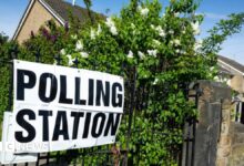 A polling station sign outside a polling station in Wakefield. The laminated sign is on metal railings surrounded by flowering shrubs