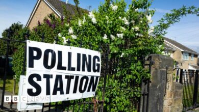 A polling station sign outside a polling station in Wakefield. The laminated sign is on metal railings surrounded by flowering shrubs