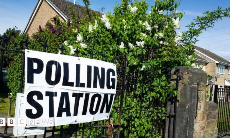 A polling station sign outside a polling station in Wakefield. The laminated sign is on metal railings surrounded by flowering shrubs