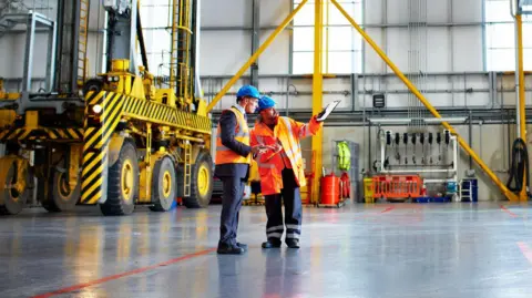 Getty Images Two men in blue hard hats stand in a warehouse