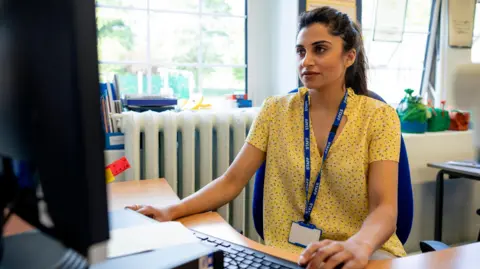Getty Images A teacher wearing a yellow shirt and a blue 