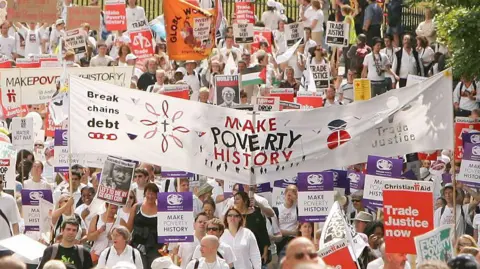 Getty Images A crowd of protesters walk through Edinburgh during the Make Poverty History march in 2005. They carry a large banner reading 