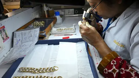 Getty Images Woman in white lab coat looks at an embellished gold ring though a jeweller's loupe at a site in India