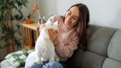 Getty Images A stock photo of a woman sitting at home with her dog