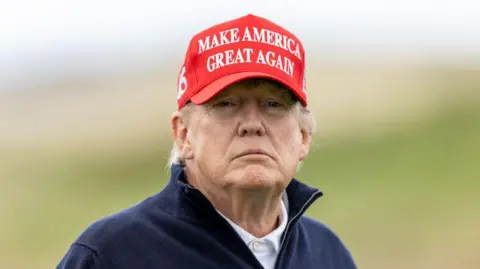 Getty Images Head and shoulders of Donald Trump, who is wearing a white polo shirt, a navy blue fleece and a red cap which says 