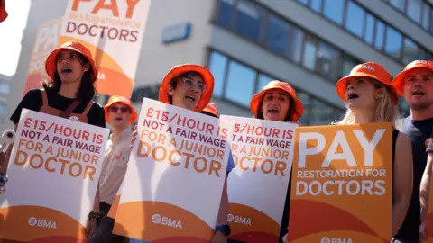 PA Media A group of junior (now called resident) doctors holding placards outside a hospital in London last year. They are holding signs saying