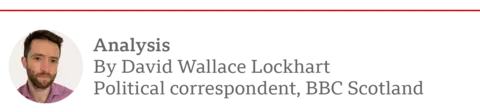 a photo of David Wallace Lockhart, a man with dark hair and dark facial hair. Next to him is text which reads