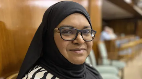 BBC Councillor Repi Begum sat in Swindon Borough Council chamber wearing thick black rimmed glasses and a hijab