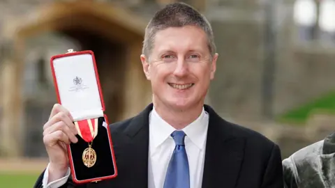 Getty Images Sir Robert Chote holds up a medal in a red box
