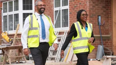 PA Media Sir James Cleverly and Kemi Badenoch visit a building site, dressed in high vis jackets