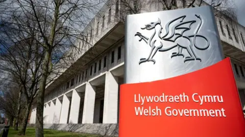 Getty Images The Welsh government's Cardiff headquarters in Cathays Park, with a large silver and red sign in front of it with the words Welsh government in Welsh and English.  The grey concrete building has columns wrapping around the ground floor and two horizontal rows of windows above it. 