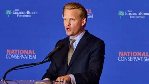 Getty Images James Orr, a man with swept back blonde hair in a dark suit and sandy tie, speaks at a podium at a National Conservatism conference in Washington DC
