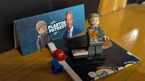 Nigel Farage Lego figure clutching a beer, against a backdrop of