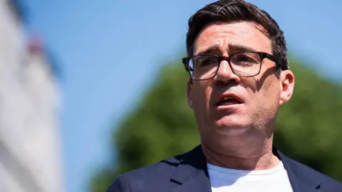 PA Media Mayor of Greater Manchester Andy Burnham wearing a white t-shirt and blue suit jacket and glasses. 
