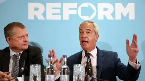 Getty Images Reform UK leader Nigel Farage - a grey haired man in a dark suit - at a press conference alongside new MSP Graham Simpson - also a grey haired man in a dark suit. They are sitting in front of a banner reading