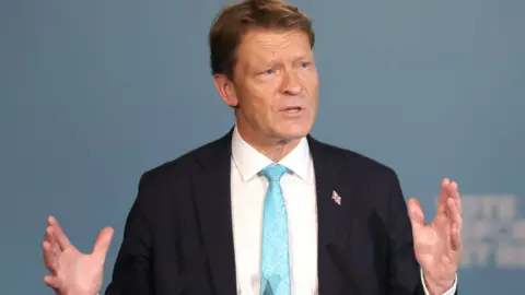 EPA Reform UK deputy leader Richard Tice wears a black suit, a white shirt and a light blue tie.